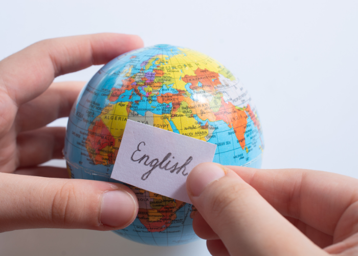 Mãos segurando um globo terrestre com um papel escrito “English”, representando o inglês como idioma global.