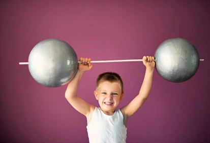 Menino sorridente levantando halteres de brinquedo, representando força e possibilidade – ideal para ensinar verbos modais em inglês.
