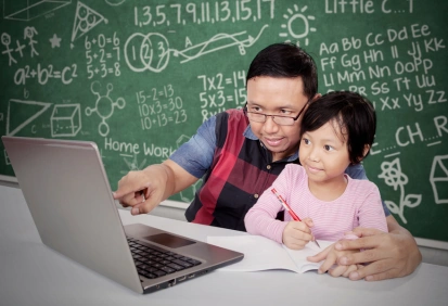 Pai ajudando a filha com lição de casa em frente ao computador, quadro-negro ao fundo – imagem ideal para ensinar o uso do modal verb “must” em inglês.