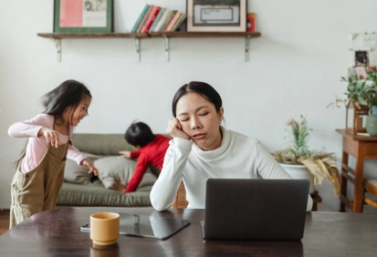 Mãe tentando trabalhar no computador enquanto duas crianças brincam no sofá – imagem ideal para explicar a diferença entre Past Continuous e Past Simple.
