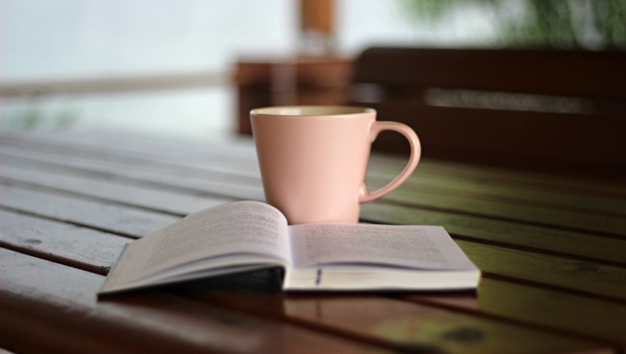 Xícara rosa e livro aberto sobre uma mesa de madeira.